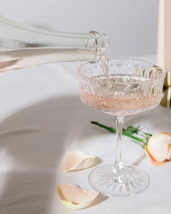 Champagne being poured into a glass with a rose and candles in the background